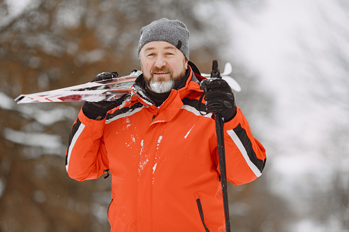 Happy mature man in winter park. Senior activewear trekking or skiing in the forest at leisure