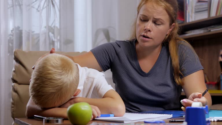 A little boy cries when doing homework at home, an angry mother shouts.