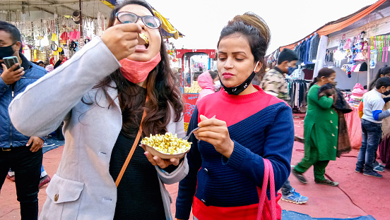Lucknow, India, January 2021 : Two girl friends eating street food (Bhelpuri) together in outdoor market at day time at lucknow
