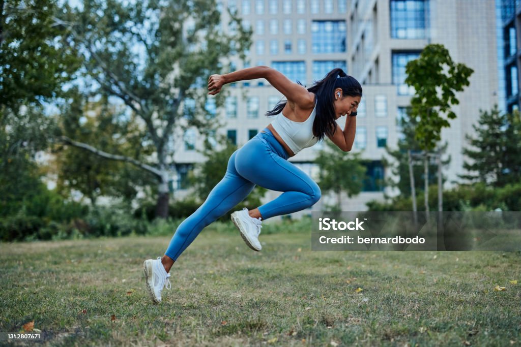 Asian woman running in park to achieve her personal best Attractive and athletic young asian woman running on a path through the park Sprint Stock Photo