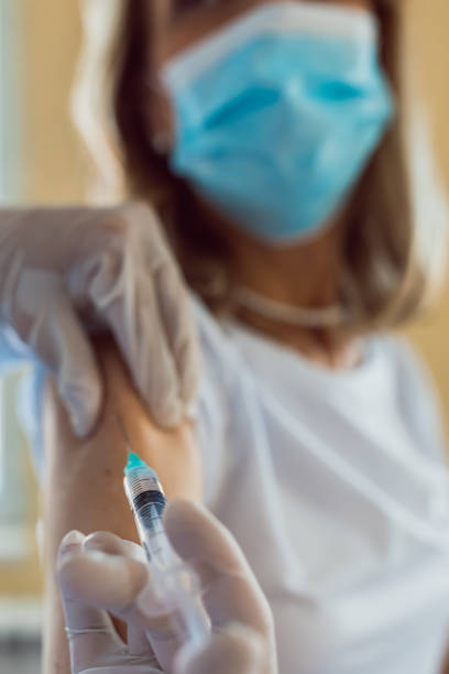 istock Close up of general practitioner hand holding vaccine injection while wearing face protective mask during covid-19 pandemic. Mature man nurse with surgical mask giving injection to senior woman. 1342810818