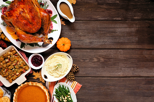 Classic Thanksgiving turkey dinner. Top down view side border on a dark wood background with copy space. Turkey, mashed potatoes, stuffing, pumpkin pie and sides.