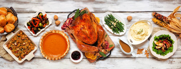 istock Traditional Thanksgiving turkey dinner above table scene on a rustic white wood banner 1342817784