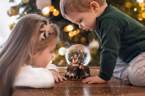 Sister and brother looking at a glass ball with a scene of the nativity of Jesus Christ in a glass ball on a Christmas tree