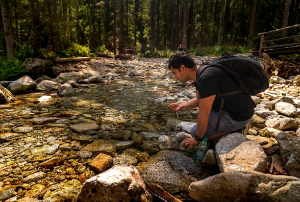 istock Tired Indian man with backpack sitting next to clean water stream or river drinking water 1342845622