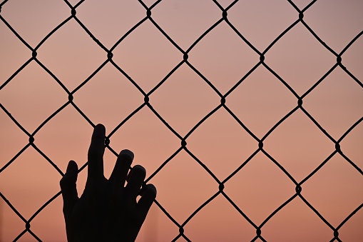 silhouette one human hand in fence, sunset background and copy space, afghanistan conflict concept