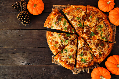 Fall pizza with pumpkin sauce, gouda and caramelized onions. Above view on a dark wood background. Copy space.