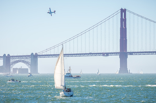 Boats sailing under the Golden Gate bridge and an airplane over it in the morning, California, USA