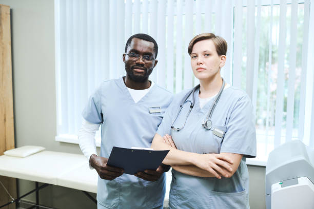 診察ソファに立って制服を着た診療所の若い多民族の同僚のチーム - scrubs surgeon standing uniform ストックフォトと画像