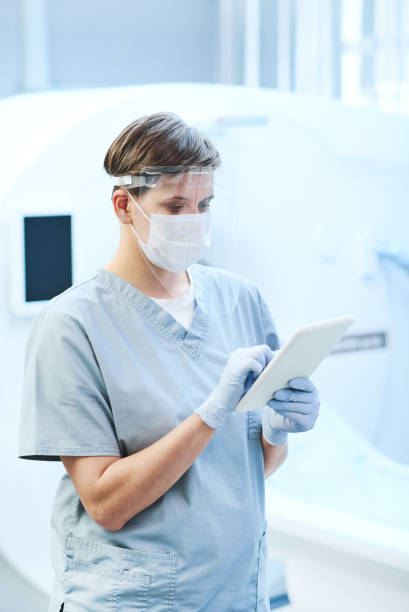 istock Busy young MRI tech in safety face shield and gloves using tablet while analyzing online CT scan of covid patient 1342881874