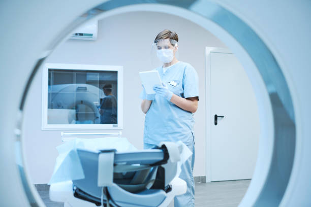 istock Serious nurse in protective mask and gloves using tablet and reading patients card while preparing MRI scanner for covid patient 1342882414