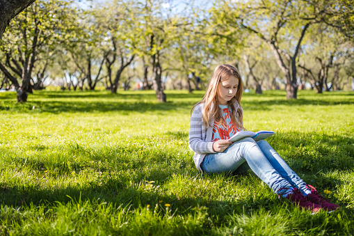 Girl lying down outdoors in a park and reading a book.