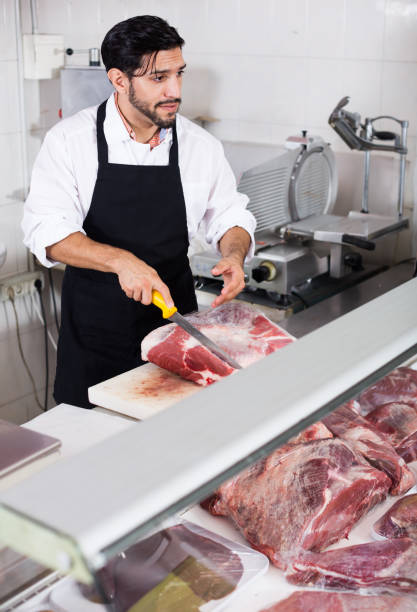 istock Brunette butcher is cutting meat for clients 1342903887