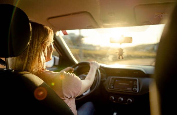 donna che guida la sua auto su una strada in un pomeriggio di fine estate - driving women rear view sitting foto e immagini stock