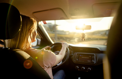Rear view of a woman driving her car on along a road on a late afternoon in the summertime