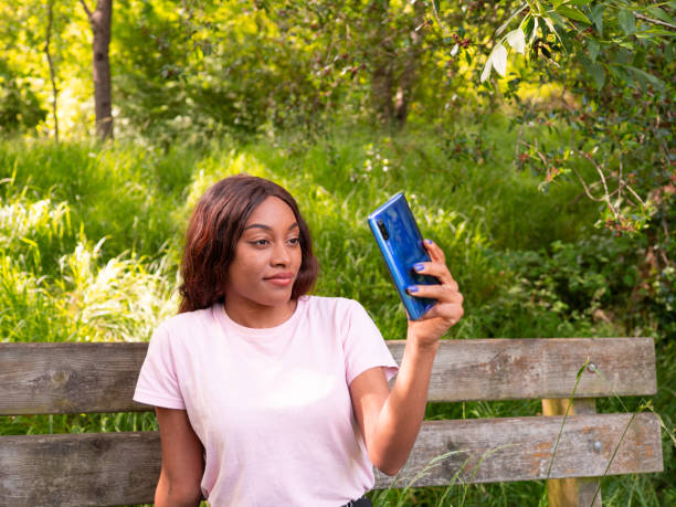 Young black woman with her phone taking selfie in a park on an October afternoon. Young black woman with her phone taking selfie in a park on an October afternoon. 15495 stock pictures, royalty-free photos & images