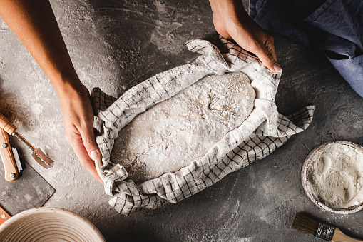 Cropped shot of a woman hands covering sourdough bread dough with a cloth for proofing. Female making sourdough bread in the kitchen counter.
