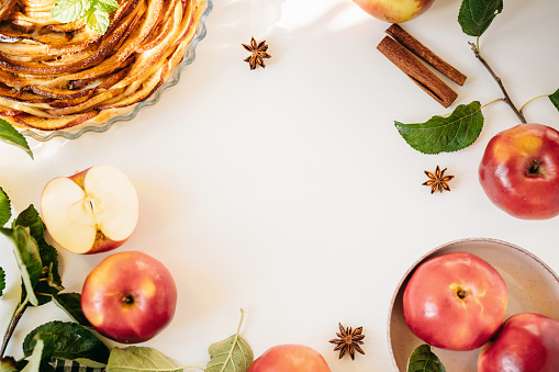 Top view of apples, spices and cake on white background with copy space