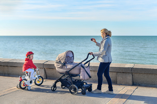 Mother with a stroller and daughter on a bicycle are walking together