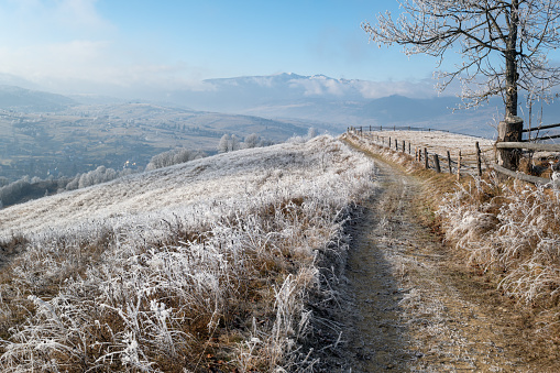 Winter coming. Last days of autumn, morning in mountain countryside peaceful picturesque hoarfrosted scene. Dirty road from hills to the village. Ukraine, Carpathian mountains.