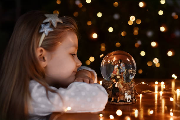 girl looking at a glass ball with a scene of the birth of jesus christ - color image jesus christ child people imagens e fotografias de stock