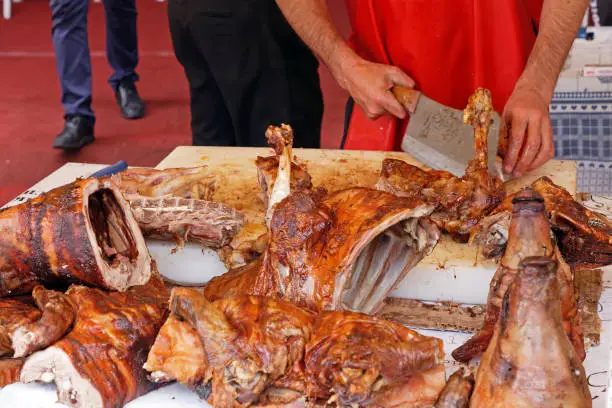 Man using clever to cut meat of lamb roasted on a spit to sell on rural market fair