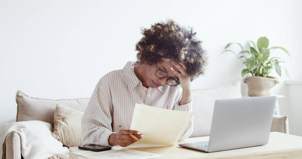istock Single young african housewife with many debts feeling stressed, calculating finances, siting at table with papers, trying to make both ends meet, not able to pay off utility bills 1342980416