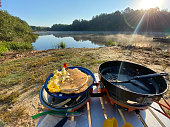 Bacon eggs and pancakes on cooking camp stove by lake
