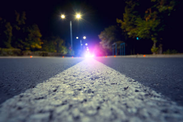 focus on city road with blurred police car red and blue lights in the distance, crime and accident concept - speeding ticket imagens e fotografias de stock