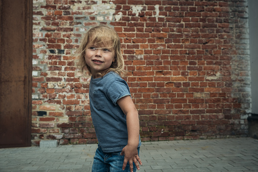 Little cute girl in a blue t-shirt and jeans with a cap is dancing on the background of an old brick wall.