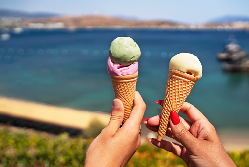 Icecream in couple hands, Female hands holding melting ice cream waffle cone in hands on summer nature background
