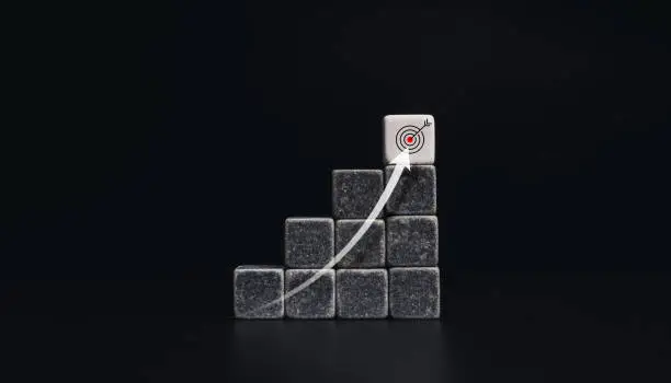 Risingup arrow from below to the top on chart steps with black and white dice blocks with target icon on dark background, minimal style. The business growth process, and economic improvement concept.