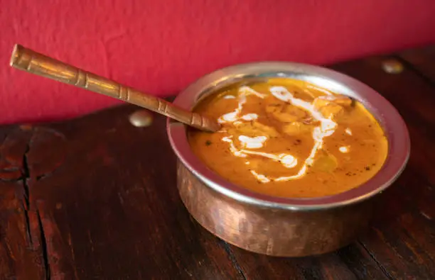 Photo of A bowl of butter chicken (murgh makhani) served on table.