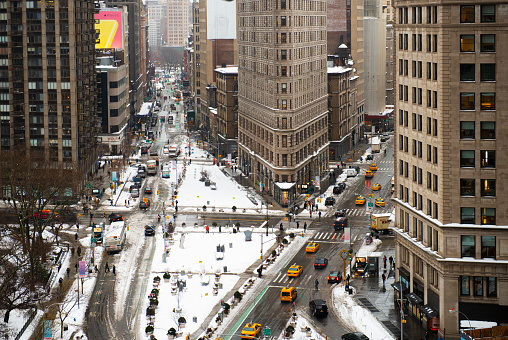 New York, New York, USA - February 14, 2014: Pedestrians and cars stroll below the Flatiron Building in winter. Finished in 1902, the landmark Flatiron Building (New York) on 5th Avenue and Broadway.