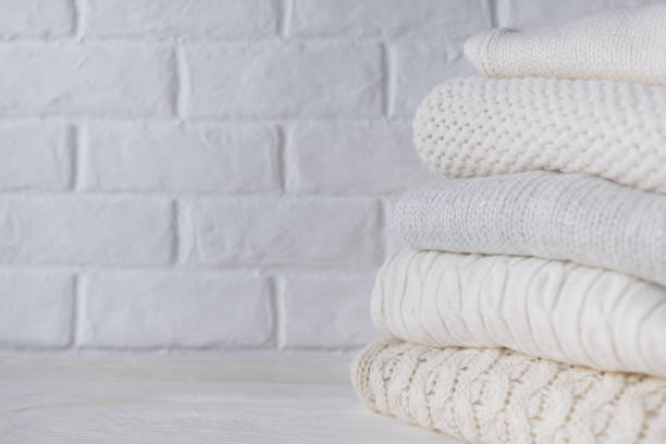 istock Stack of white cozy knitted sweaters against the background of white brick wall. 1343076114