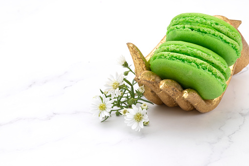 Two green macaroons on a gold wooden hand with tiny white flowers. Marble top background.