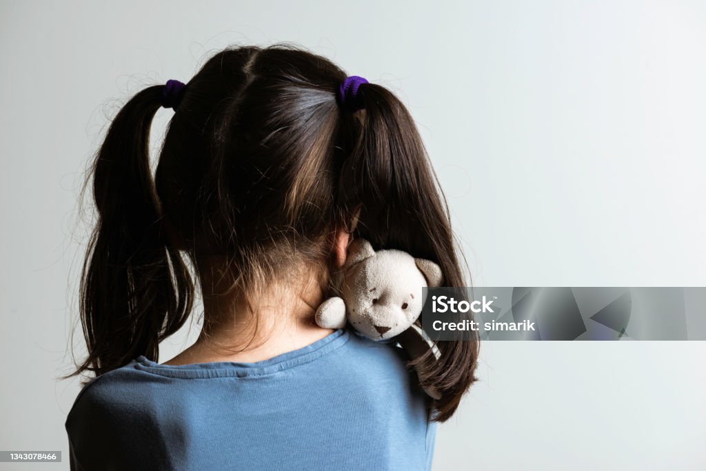 Fear Back view of little caucasian girl who is hugging her teddy bear in fear. Representing child abuse and domestic violence. Child Abuse Stock Photo