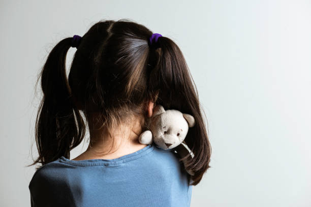 Fear Back view of little caucasian girl who is hugging her teddy bear in fear. Representing child abuse and domestic violence. child abuse stock pictures, royalty-free photos & images