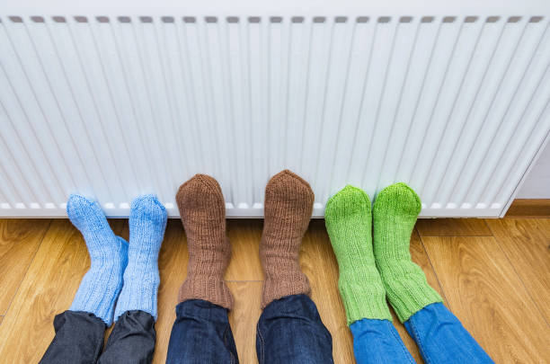 famille portant des chaussettes en laine chaude tricotée réchauffant les pieds froids devant un radiateur blanc à la maison froide. - gas boiler photos et images de collection
