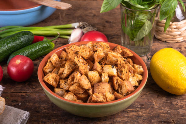 crackers in a bowl on a wooden table with salad ingredients: tomatoes, onions, cucumbers, herbs, basil and lemon - kruton stok fotoğraflar ve resimler