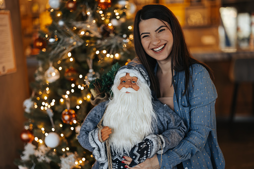 Beautiful young woman enjoying Christmas decoration, holding Santa Claus toy and smiling