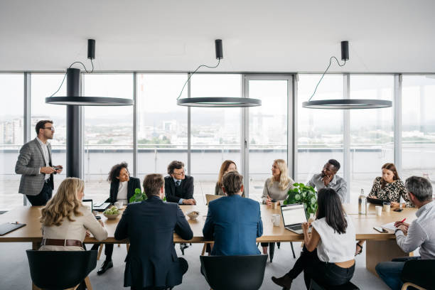 Business meeting in a bright office A photo of a business meeting in a modern office with large windows. A businessman is standing up while his colleagues are sitting down. They are smartly dressed. Horizontal daylight indoor photo. business meeting stock pictures, royalty-free photos & images