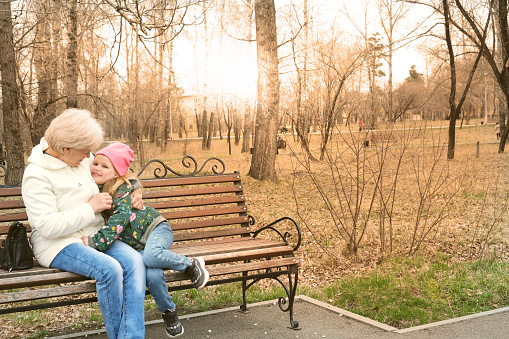 Grandmother with her granddaughter hugging and talking  sitting on a bench in the park