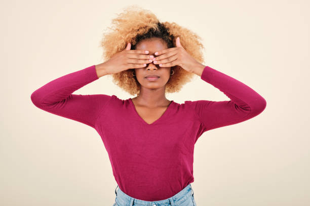 Serious afro woman covering eyes with hands while standing on isolated background. Serious young afro woman covering eyes with hands while standing on an isolated background. hair covering eyes stock pictures, royalty-free photos & images