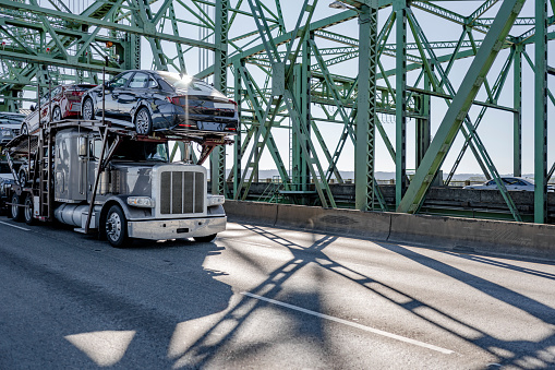 Industrial car hauler big rig gray semi truck transporting cars on modular semi trailer running on the truss Interstate Columbia River Bridge