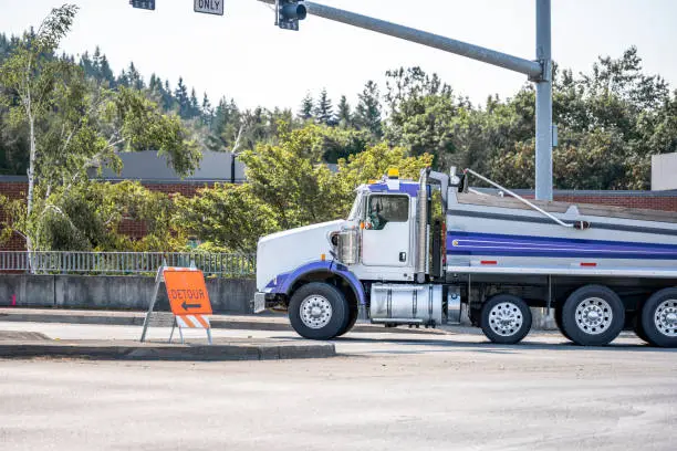 Photo of Powerful tip truck with covered trailer running on the city street crossroad with traffic light and detour road sign