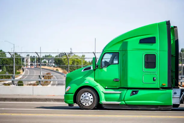 Photo of Profile of the big rig green semi truck with sleeping cab compartment running on the bridge overpass the highway road