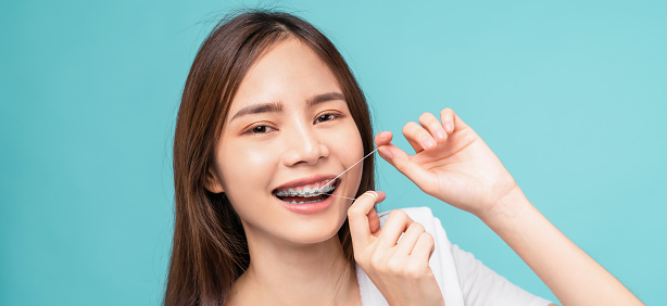 Smiling Asian woman cleaning braces on teeth with dental floss on blue background, Concept oral hygiene and health care.