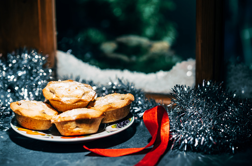 Plate of Christmas mince pies on a window ledge with view to a snowy frozen outside.