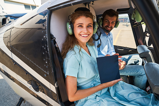 High-spirited young female with helicopter pilot certificate sitting by her smiling pleased male flight instructor